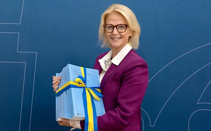 En kvinna håller i ett antal böcker med ett blågult band omkring.