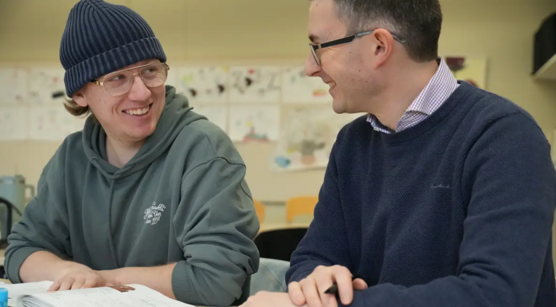 Ung man med mössa får hjälp av en lärare.